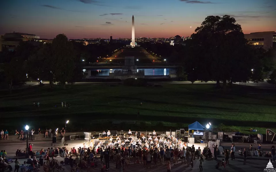A crowd at night with the Washington Monument in the distance.