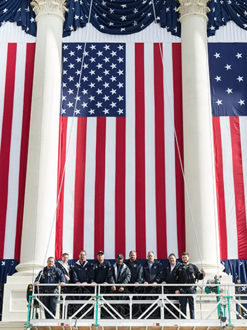 Employees of the Architect of the Capitol pause to stand in front of a flag during inauguration set up.