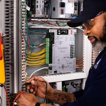 A/C Equipment Mechanic Horatio Evans tests for signal across two wires with a digital multimeter while troubleshooting air handling unit controls.