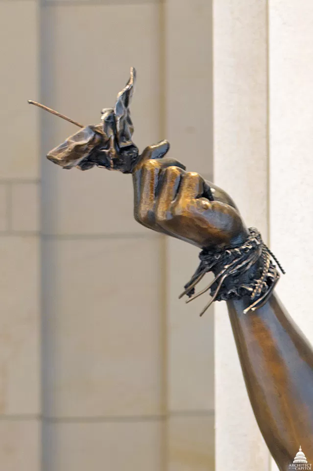 Sculpture detail of a person's hand and arm.