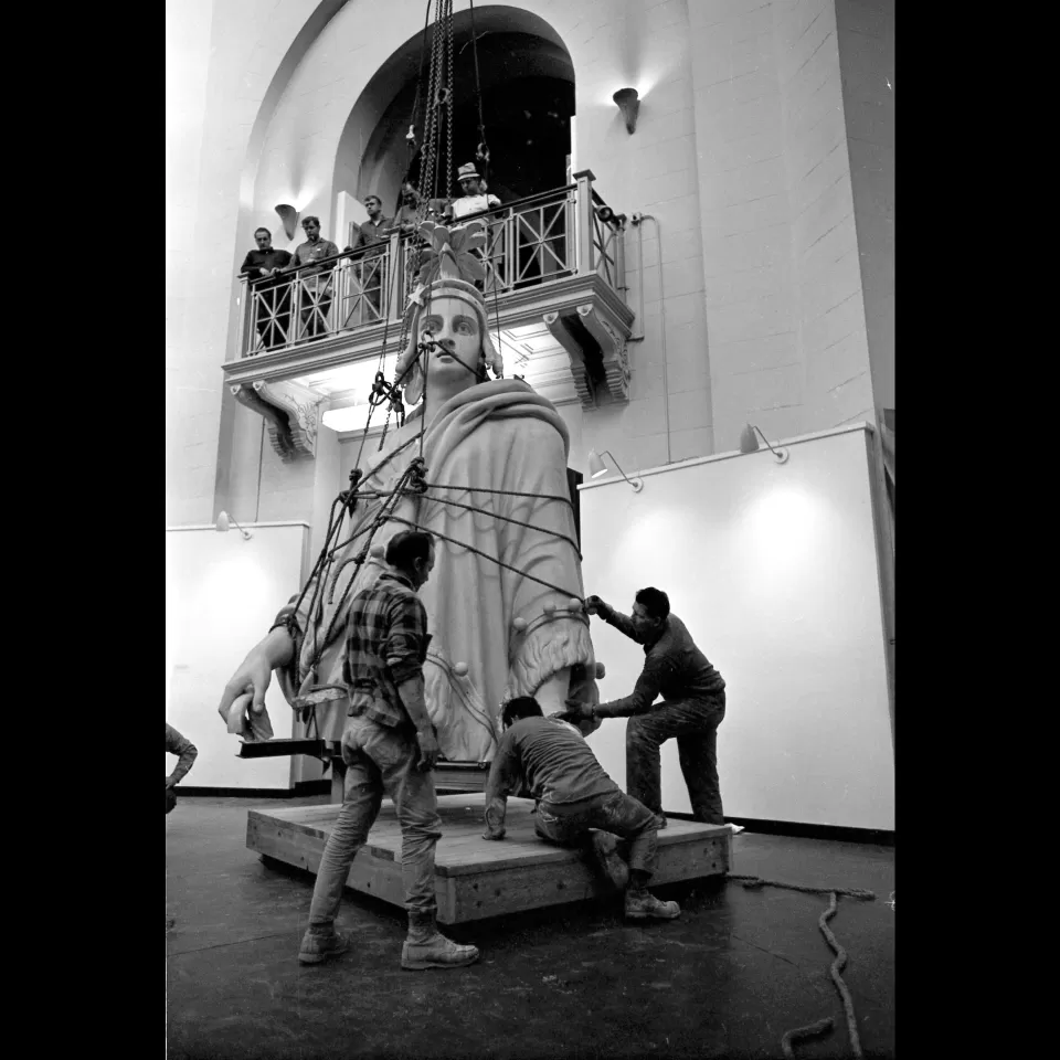 Statue being moved with people on balcony above.