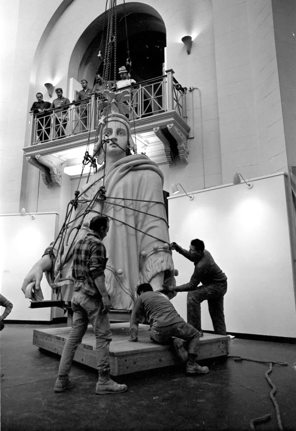 Statue being moved with people on balcony above.