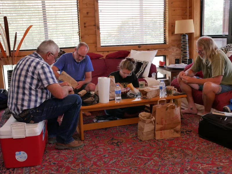 A group of four people gather around a coffee table to clean plant seeds.