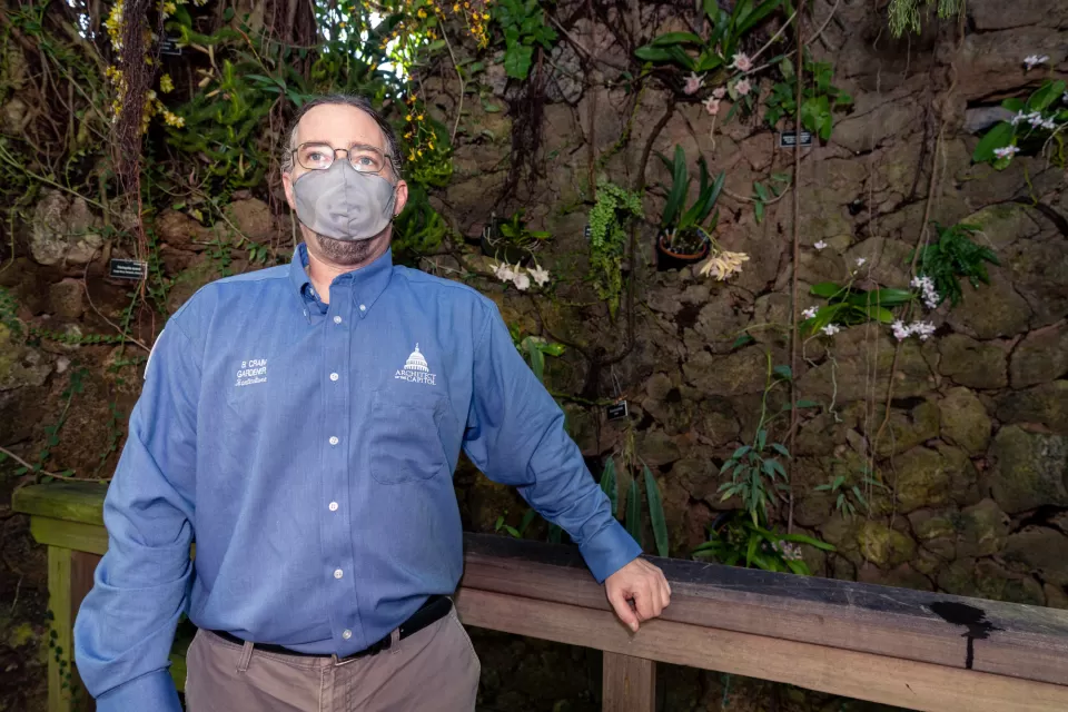 Orchid Gardener Benjamin Crain pauses for a photo in front of a wall he renovated in the Orchids house. 