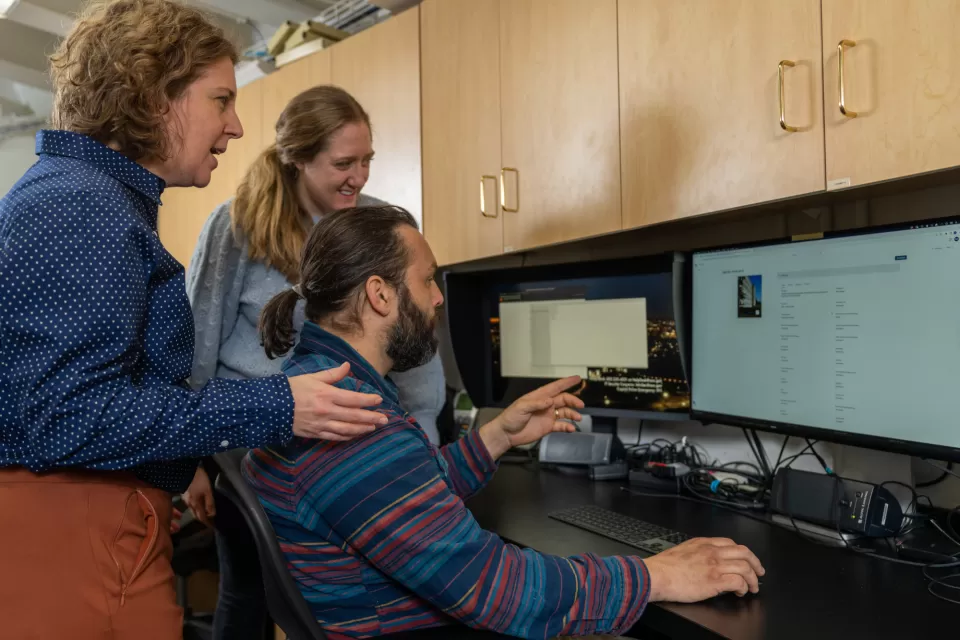 Three people facing a computer monitor.