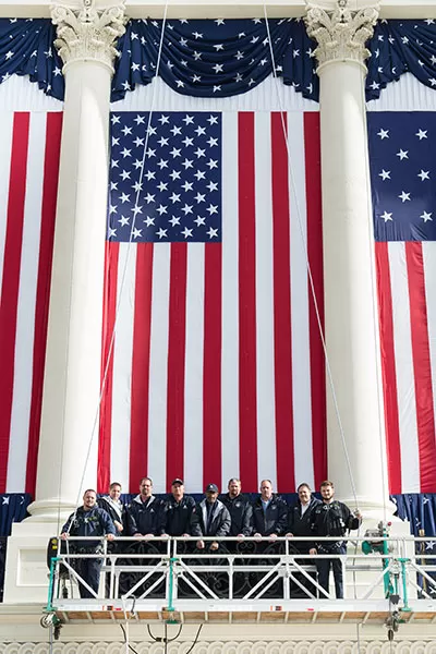 Employees of the Architect of the Capitol pause to stand in front of a flag during inauguration set up.