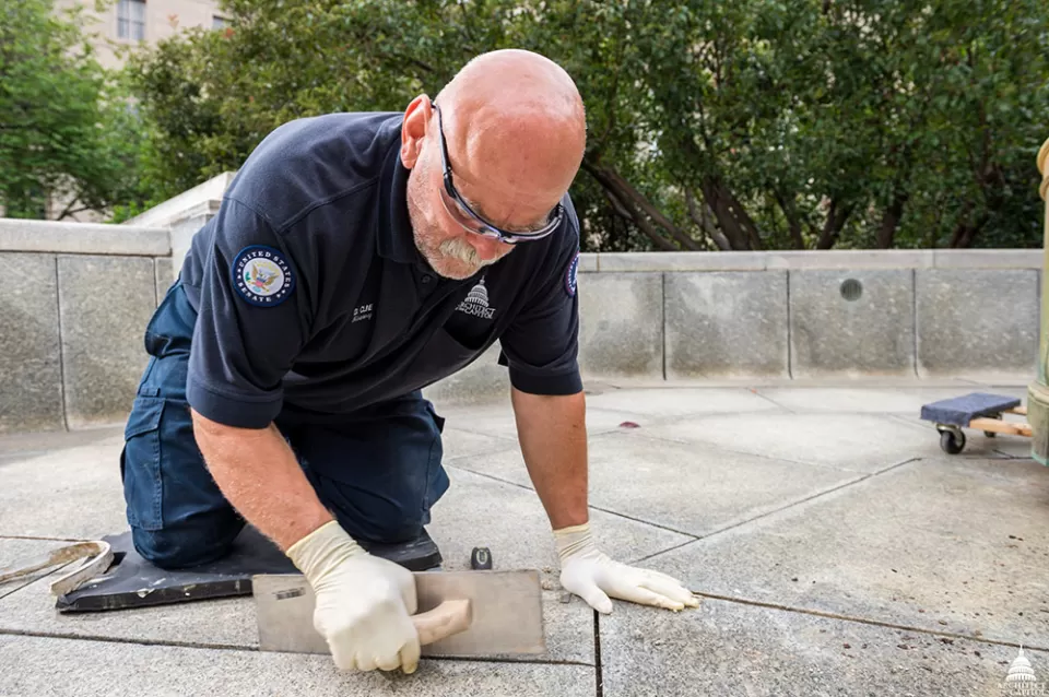 Donald Kline removes failing caulking from the Russell Courtyard fountain.