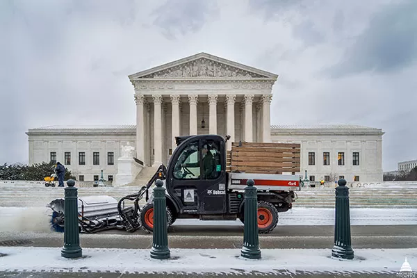 Members of the Architect of the Capitol team clear snow in front of the Supreme Court Building.