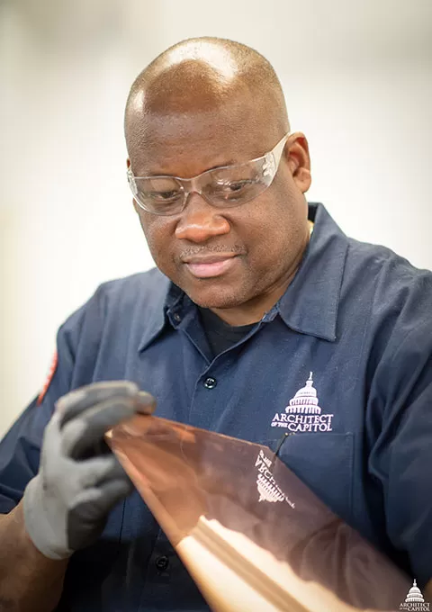 A member of the AOC's Capitol Building Sheet Metal Shop examines a piece of metal.