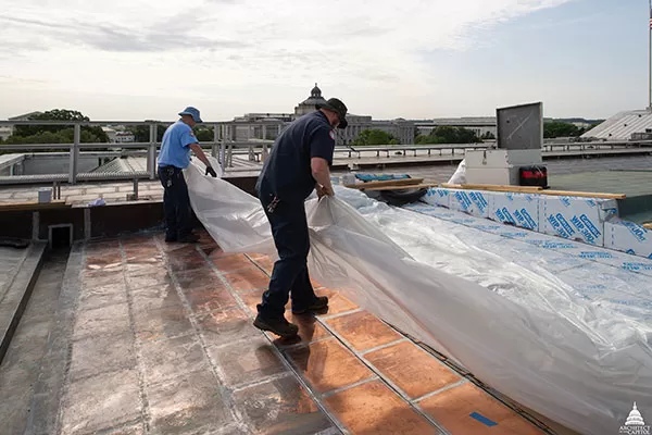 Members of the AOC Sheet Metal Shop cover the newly placed copper with plastic sheeting at the end of their shift.