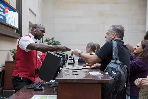 A visitor assistant hands a guest their tour badge at the U.S. Capitol Visitor Center info desk.