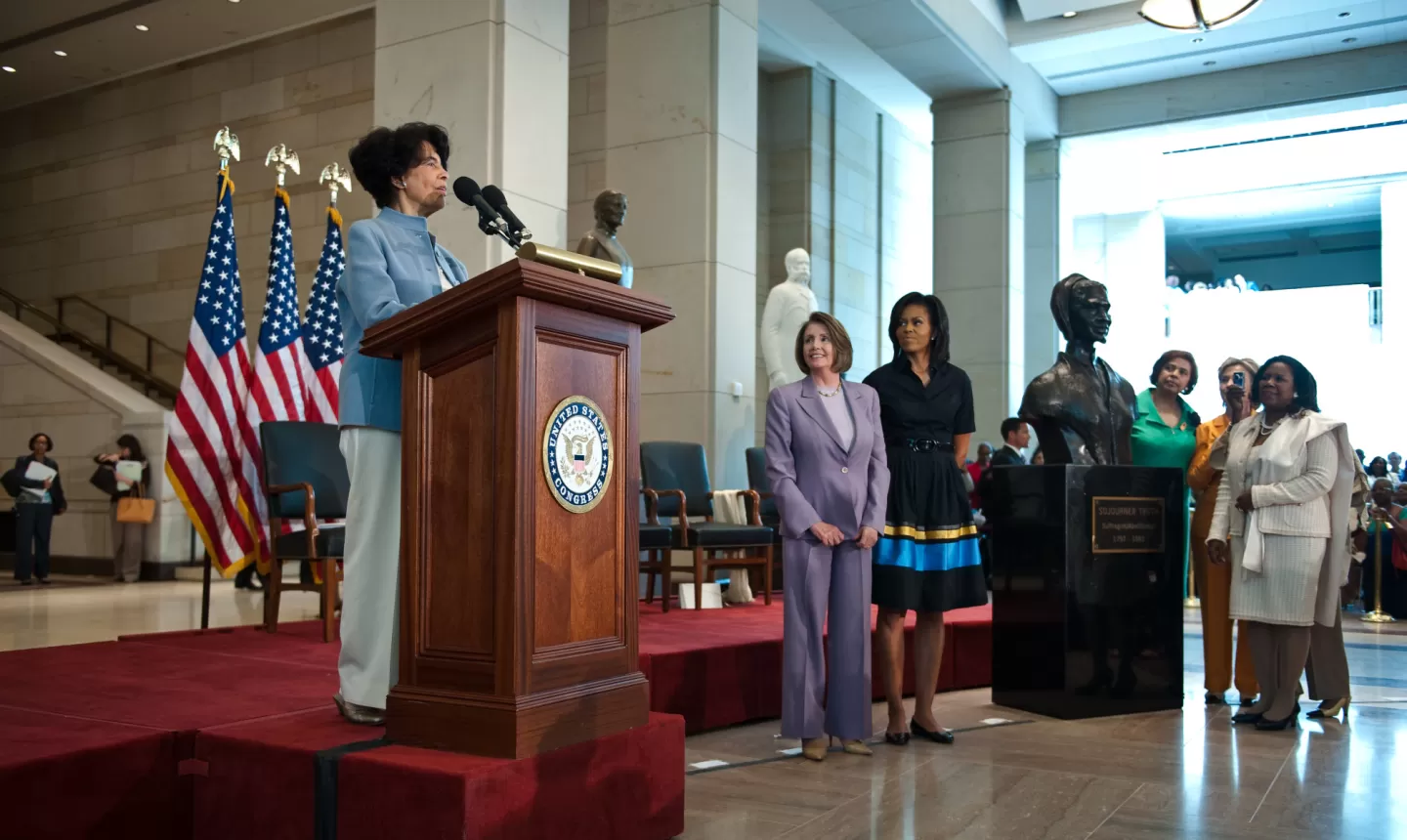 Person standing at podium with flags behind.