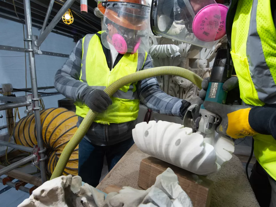 A worker carves a marble replacement leaf for a column capital.