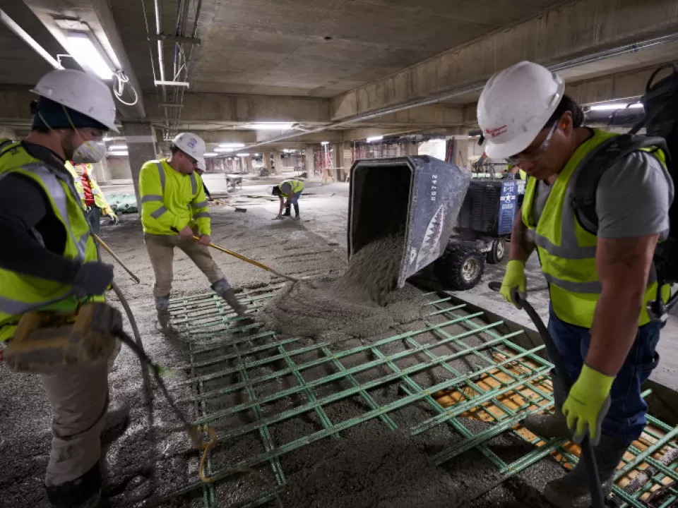 Workers apply high-strength, durable concrete on top of epoxy-coated reinforcement bars.