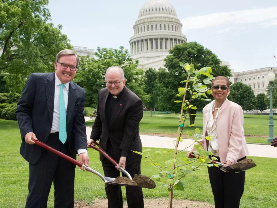 People holding shovels around a tree.