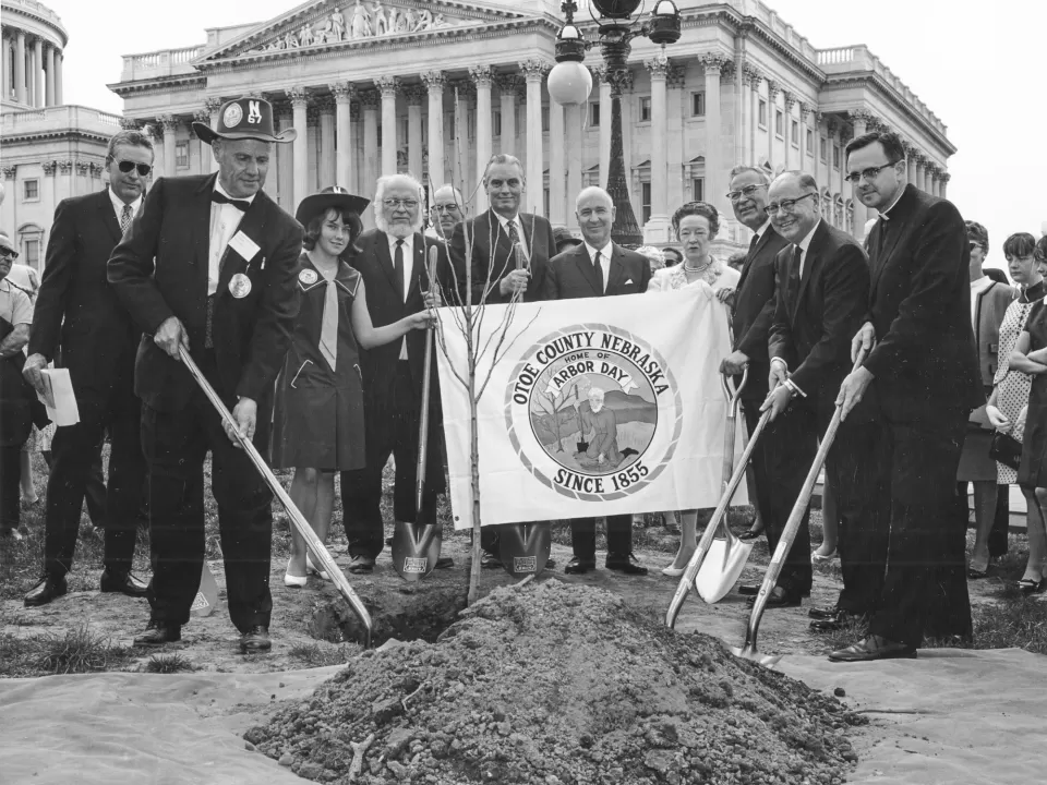 People holding shovels around a tree.