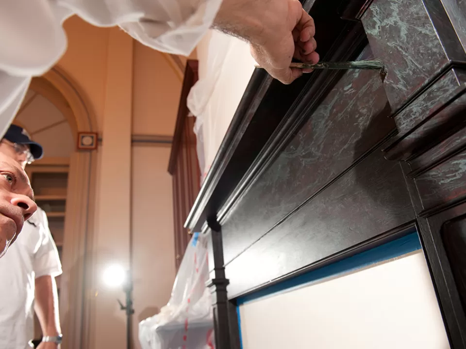 Roberto Duglio, AOC Capitol decorative painter, creates a "marble" fireplace from wood through skilled application of the right colors and design.