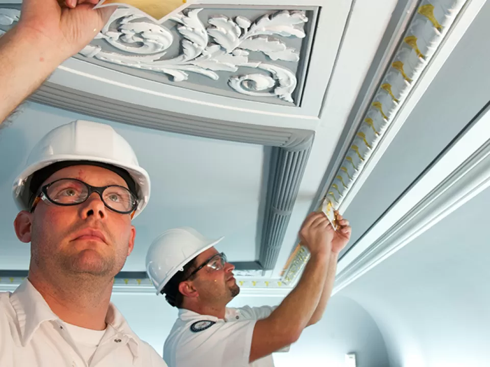  Timothy Steadman and Charles Taylor, AOC Senate painters, carefully apply gold leafing within a Senate Committee room. 