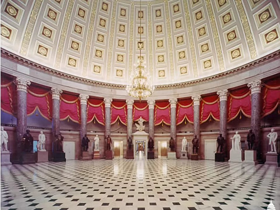 Columns in a room with statues and a chandelier.