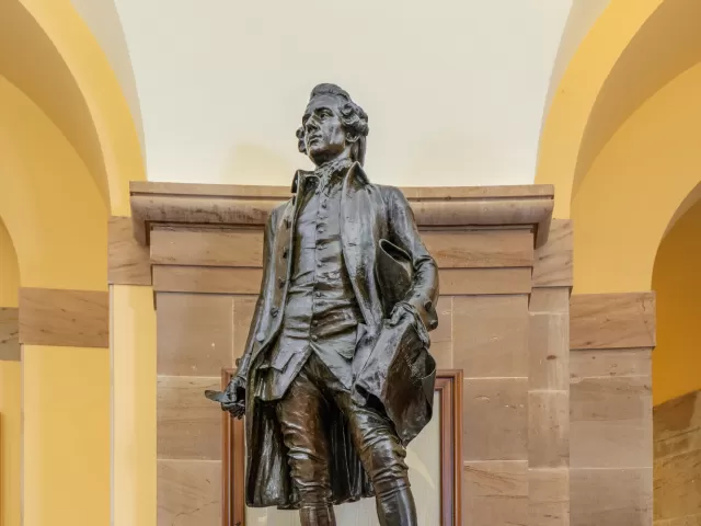 Bronze statue in front of stone wall.