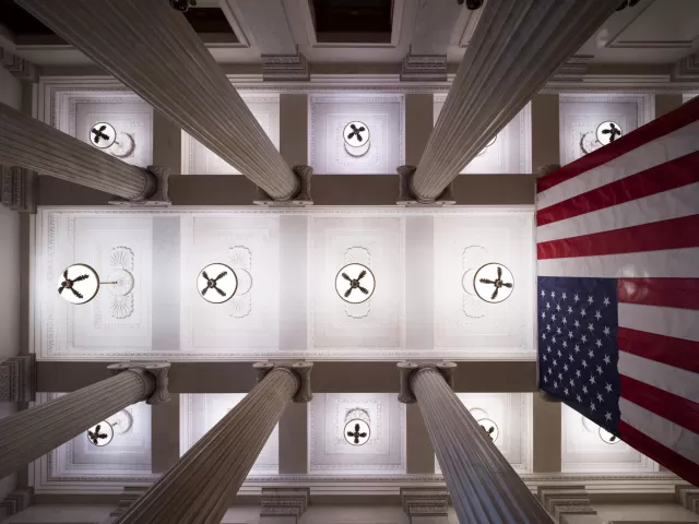 View looking up at ceiling lights, columns and the flag of the United States.