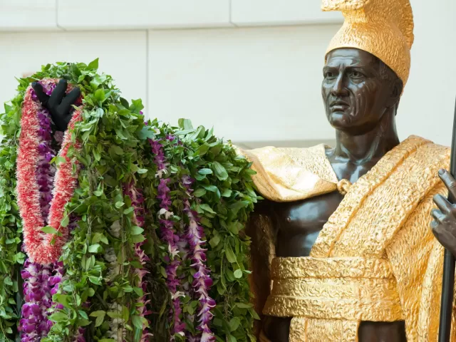 Bronze statue of a person standing holding plants.