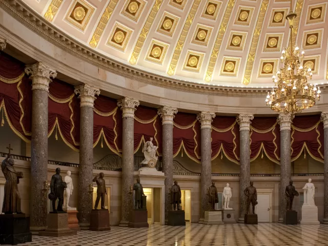 Columns in a room with statues and a chandelier.