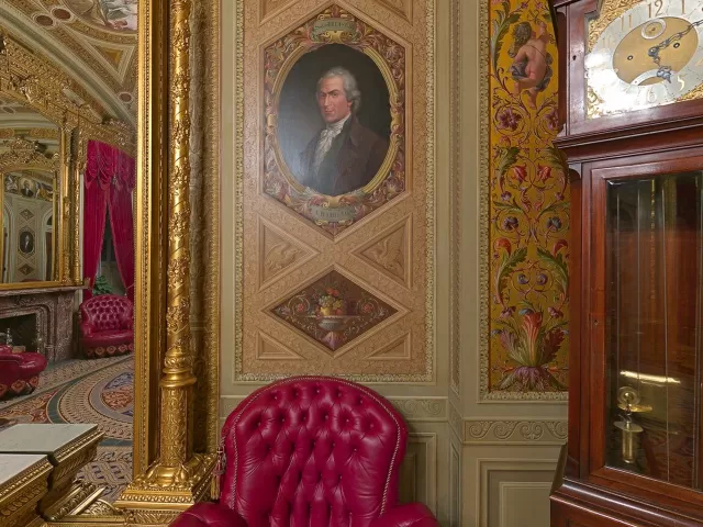 A room with a portrait, chair and clock.